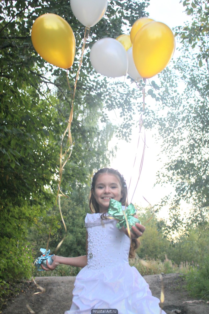 Фотография, девочка с праздничными шарами идёт по лесной дороге и протягивает шары зрителю.