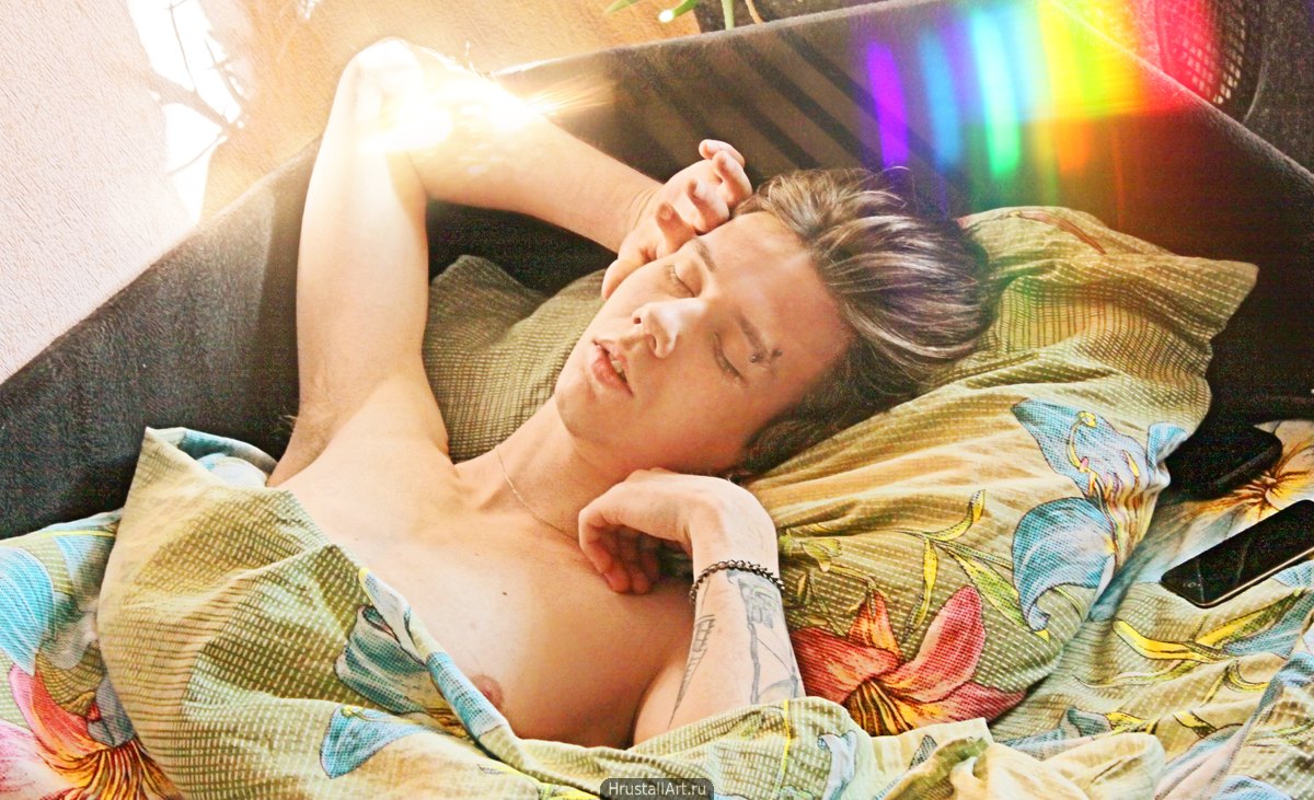 Фотография, спящий в постели парень с тату, пирсингом и радужным бликом.
