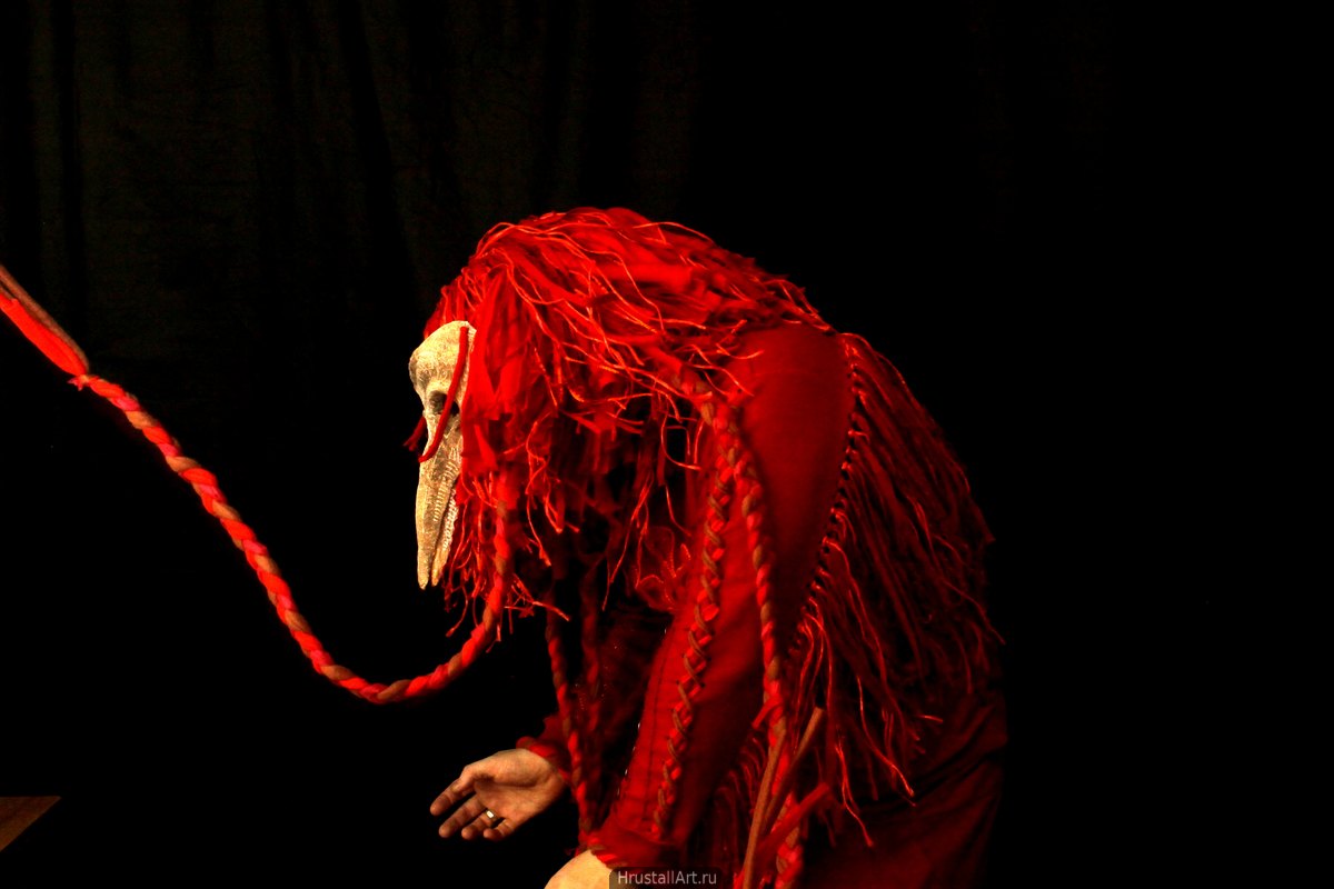 Сгорбленная фигура в красном костюме птицы.