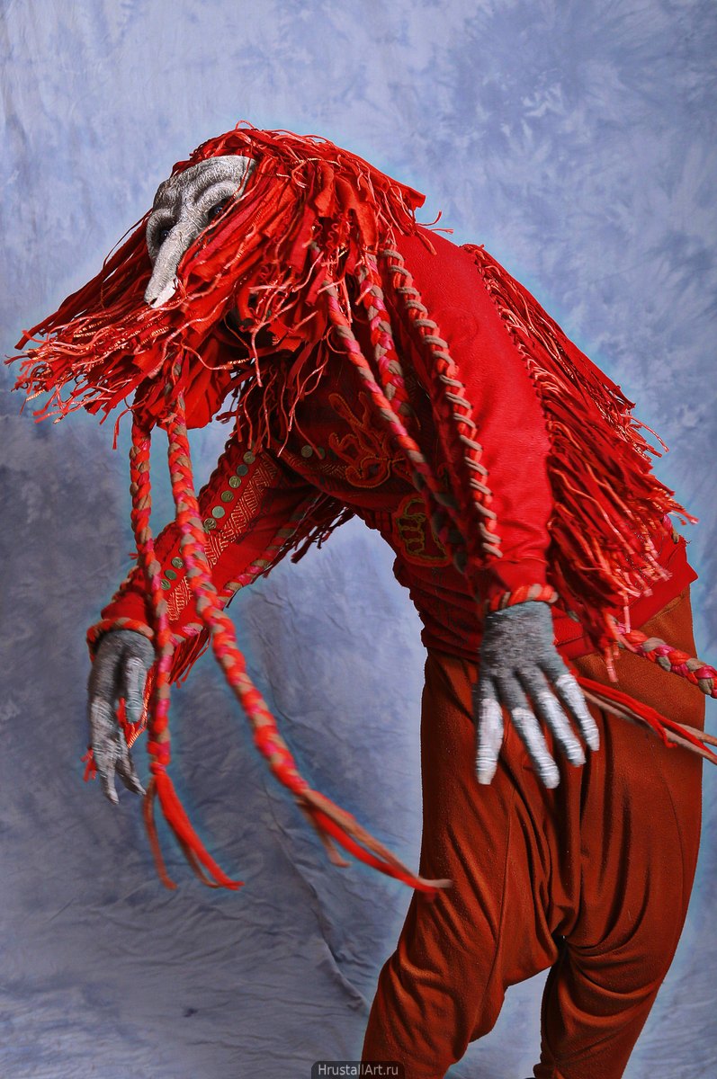 Актёр в шаманском костюме красной птицы кружится.