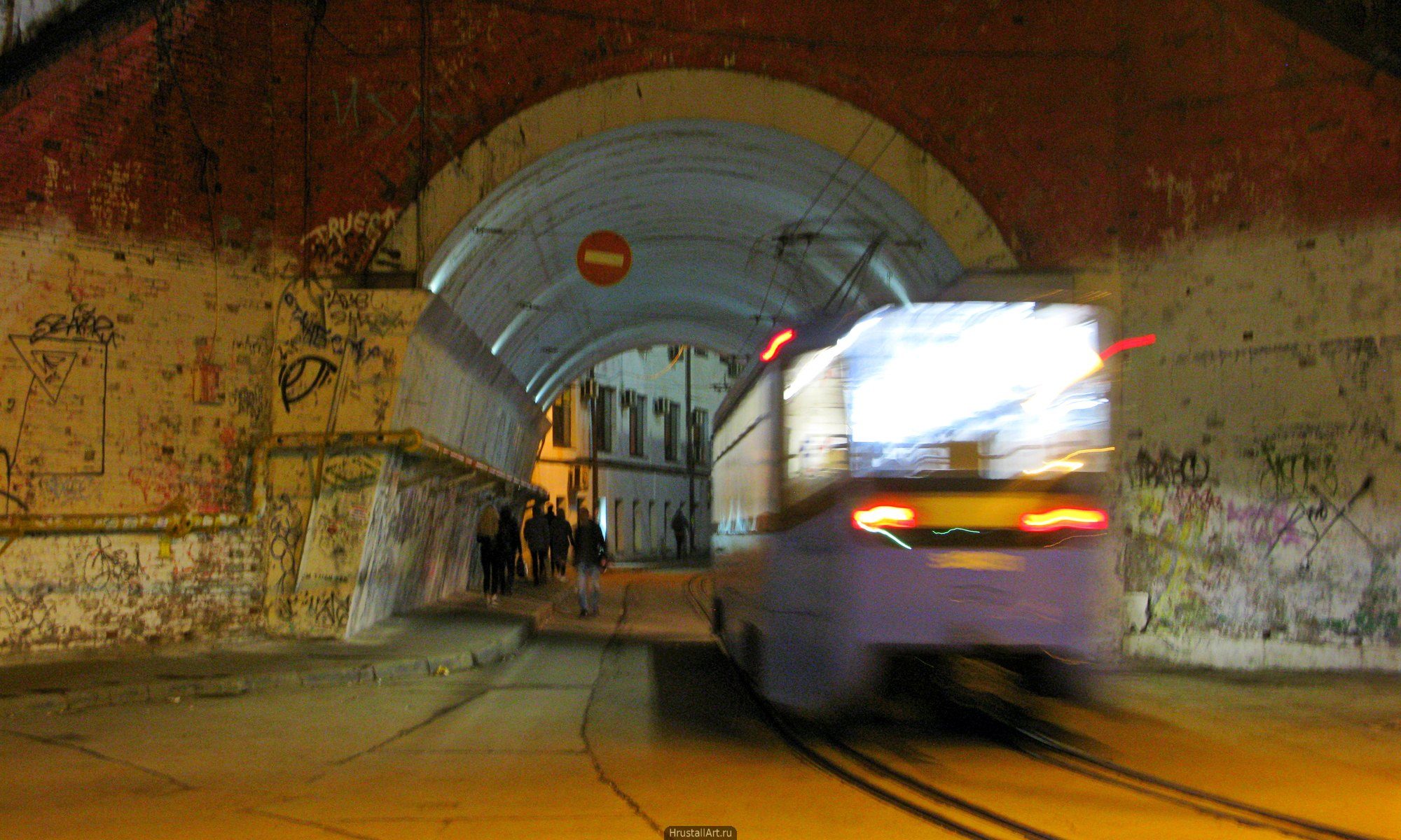 Ночной трамвай. Массивная арка проезда, вечерний свет, размытость трамвая от движения и длительной выдержки.